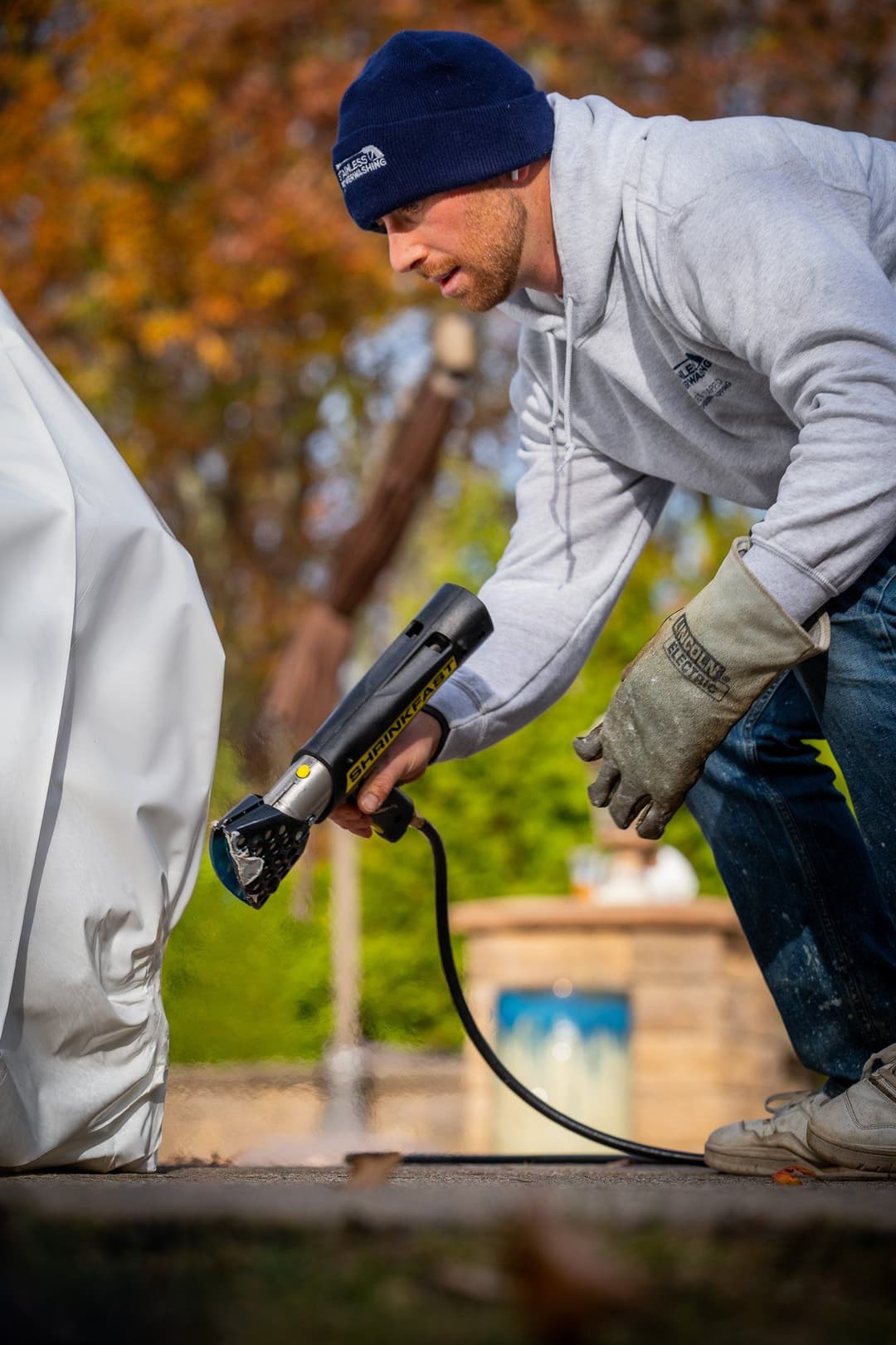 Man using a heat gun to remove a cover from outdoor furniture in a backyard setting.