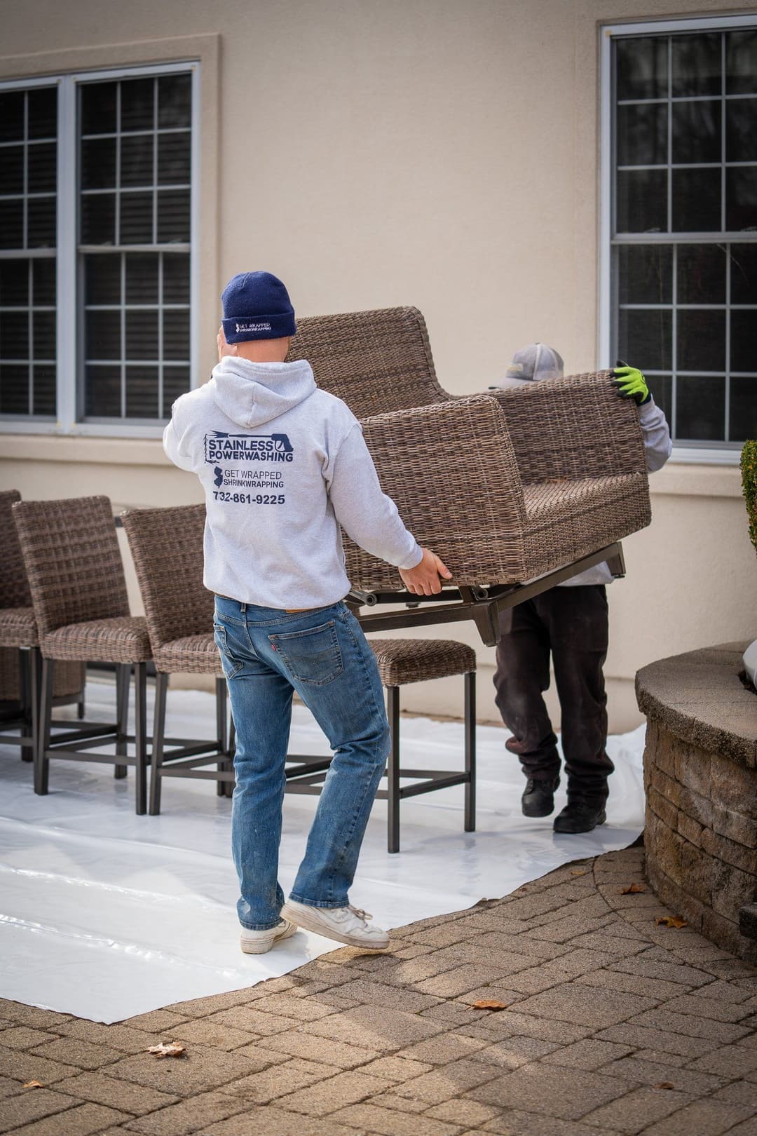 Workers moving outdoor furniture onto a patio with a white protective cover.