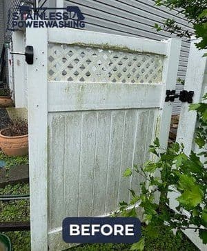 Dirty white gate with algae and grime before power washing, surrounded by greenery.