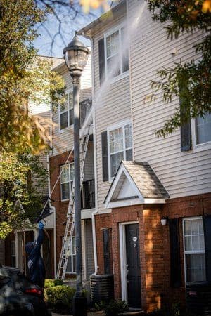 Pressure washing a residential building exterior with a ladder and water spray.