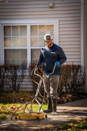 Man using a pressure washer to clean a walkway outside a residential building.