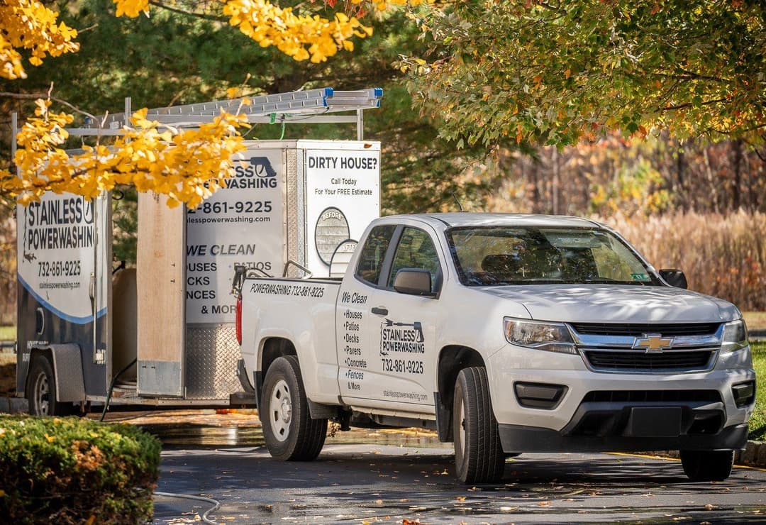 Chevrolet truck with power washing service trailer among autumn leaves. Contact for estimates.