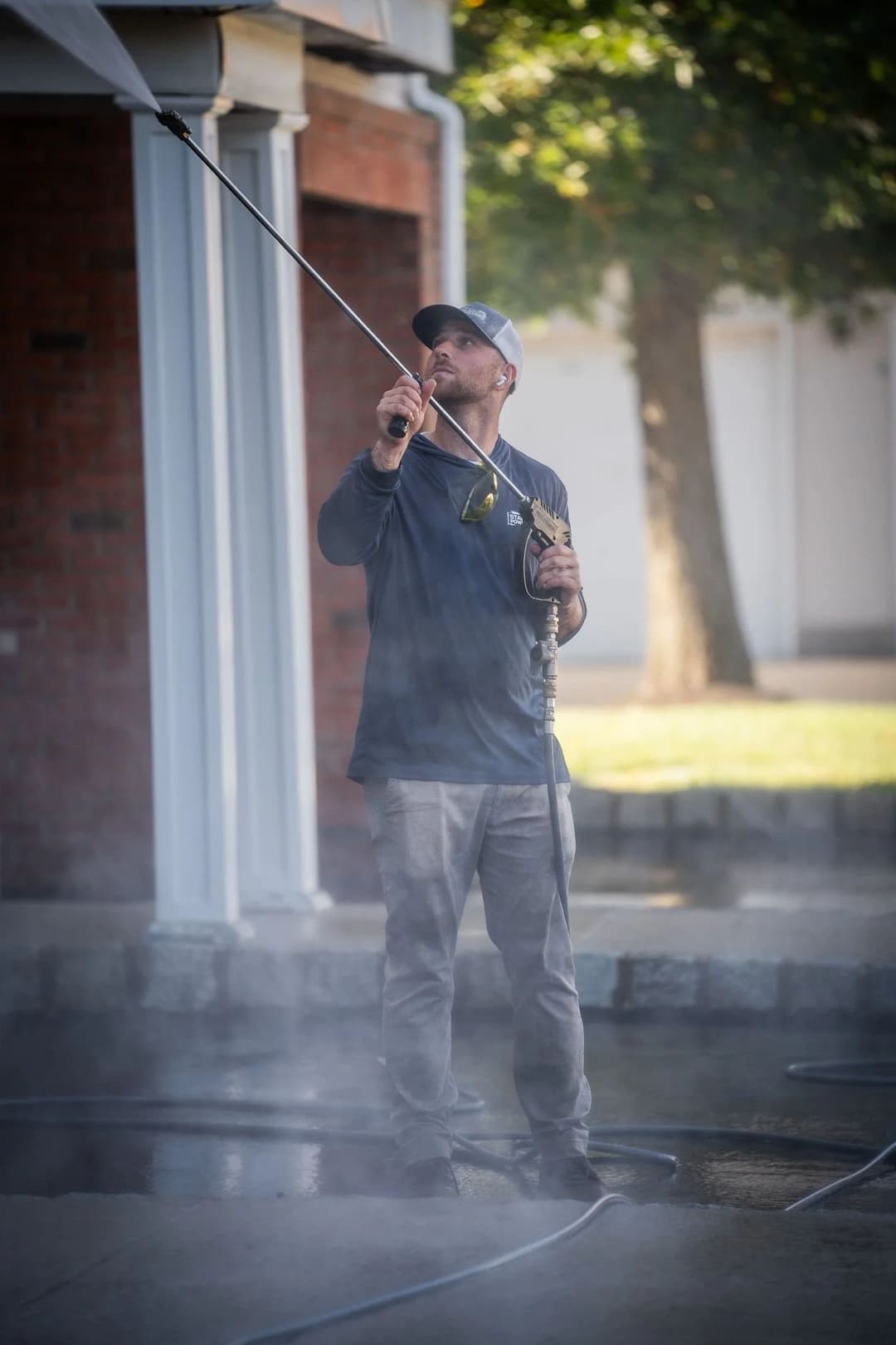 Man pressure washing a surface outdoors, surrounded by mist and greenery.