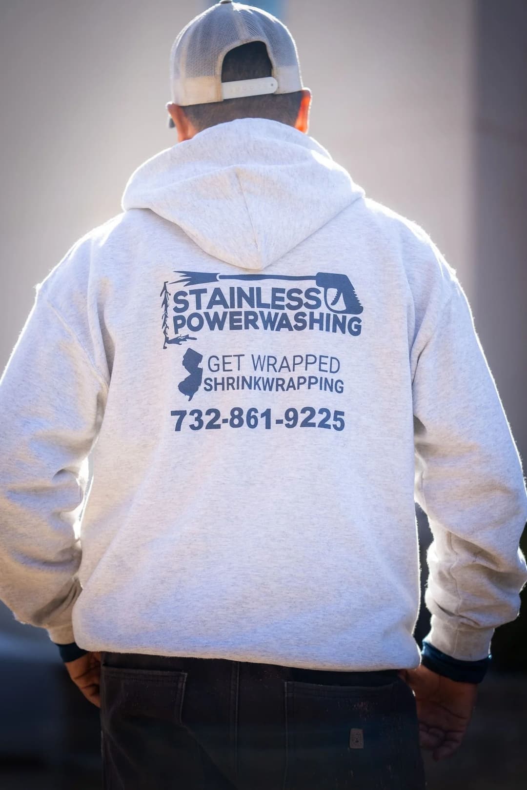 Person wearing a gray hoodie with "Stainless Powerwashing" and contact info on the back.