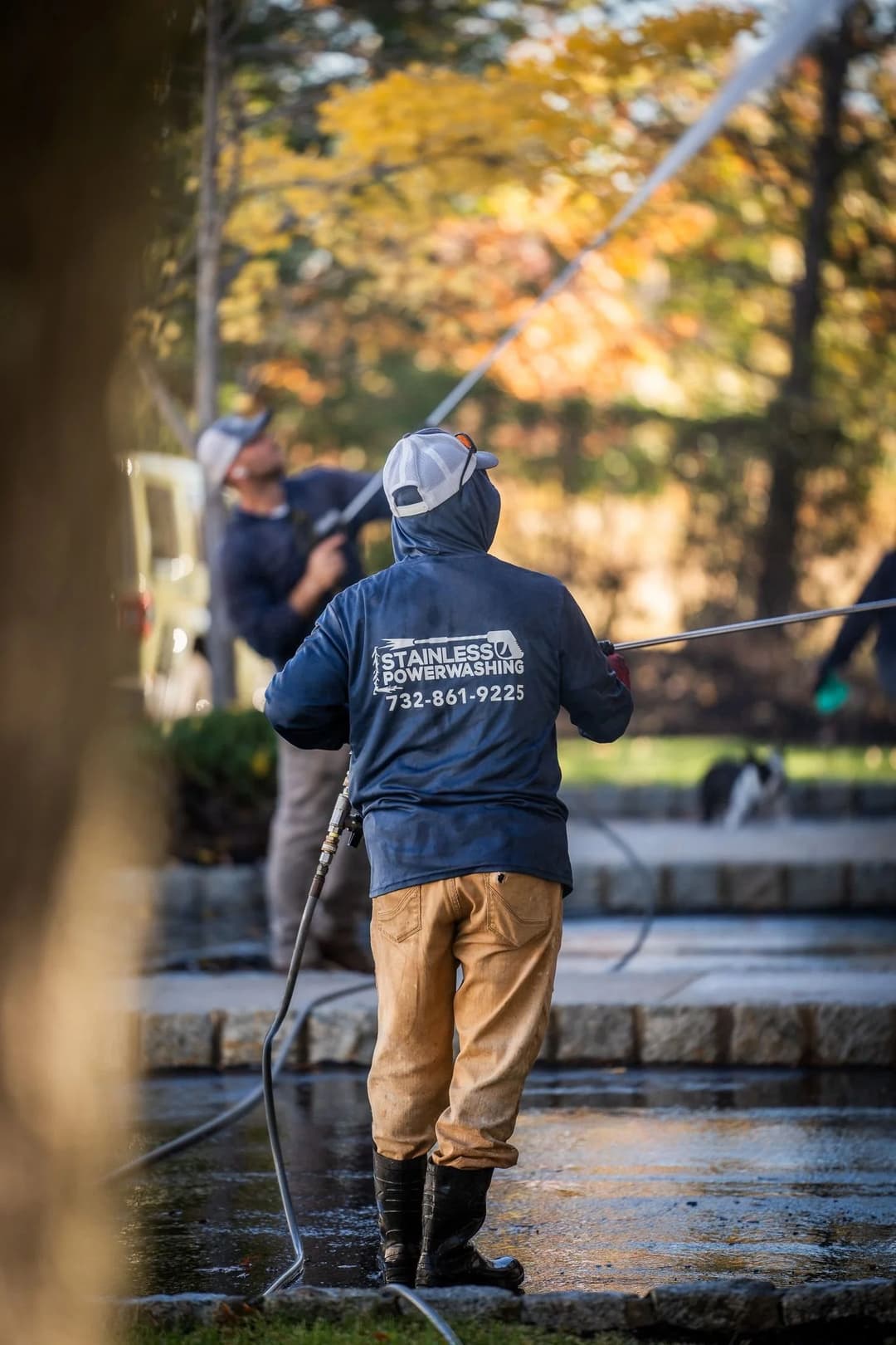 Power washing service in action, worker cleaning outdoor surface with high-pressure equipment.