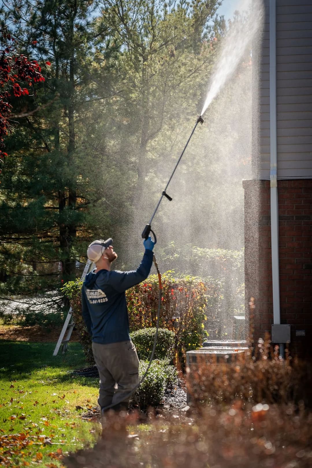 Man using a pressure washer to clean the exterior of a house on a sunny day.