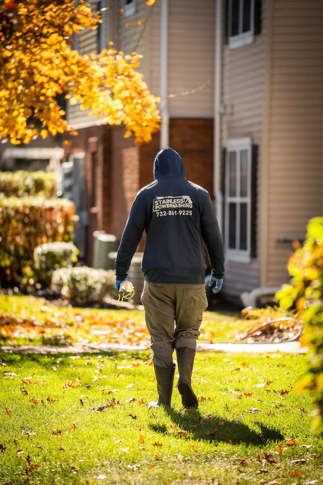Landscaper in a hoodie and gloves walking through a leaf-strewn yard in autumn.