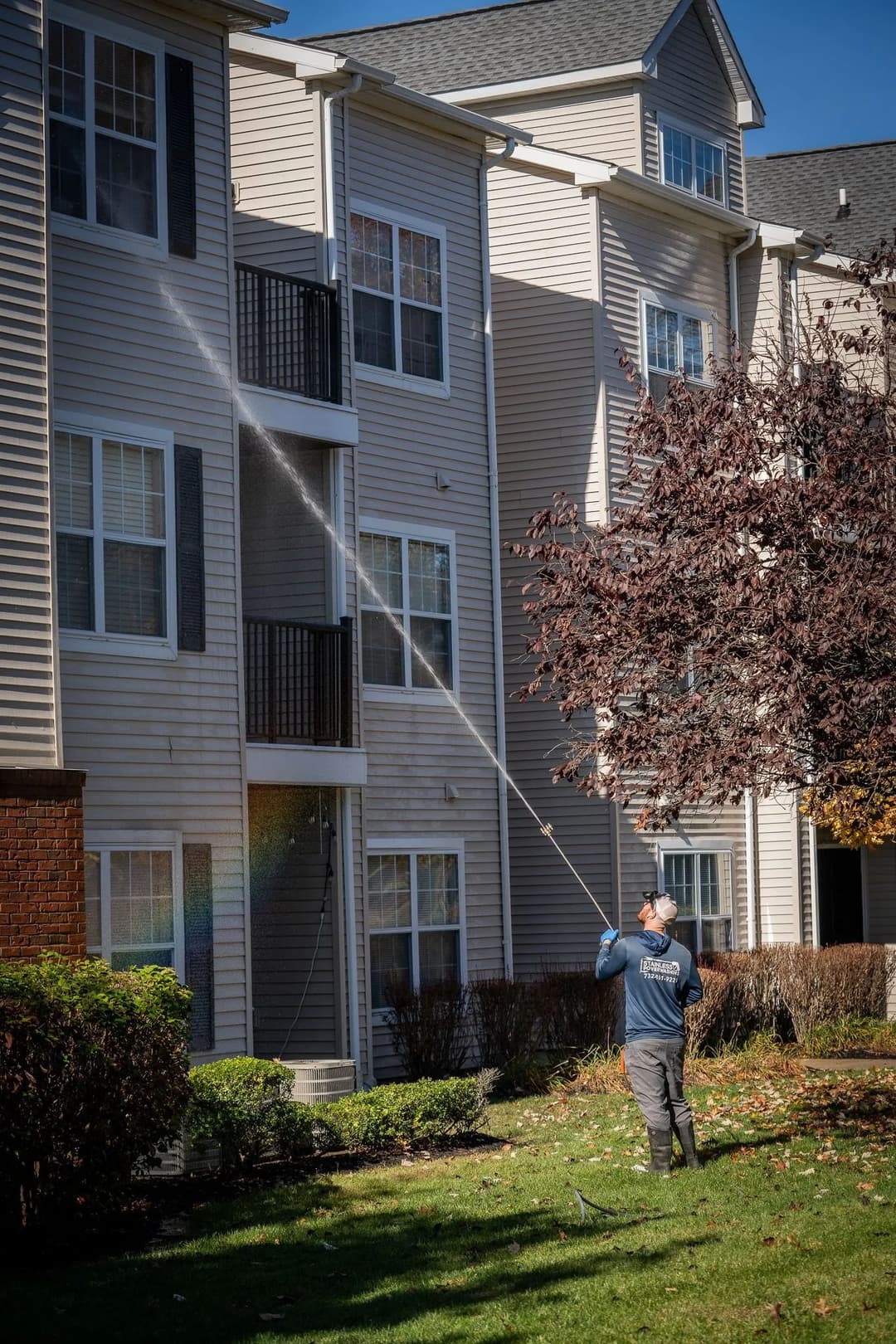 Man cleaning an apartment building exterior with a pressure washer on a sunny day.