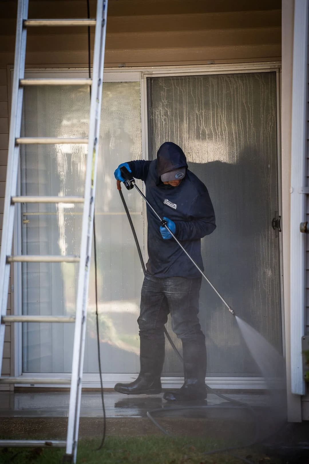 Person using a pressure washer to clean a patio with a ladder nearby.